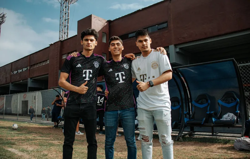 Three young men in Bayern Munich jerseys smiling at a soccer stadium, showcasing sports fandom. (stock photo via Pexels)