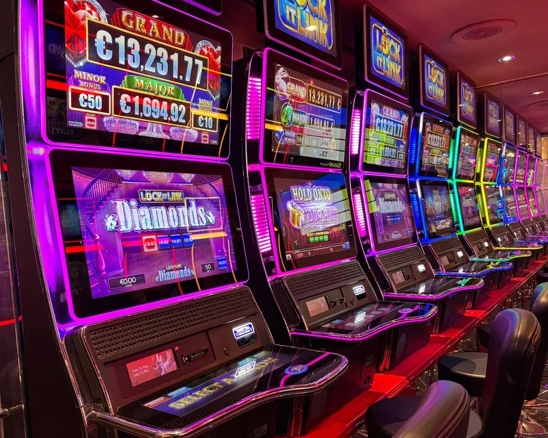 Colorful slot machines lined up in a casino with neon lights and jackpot displays. (stock photo via Pexels)