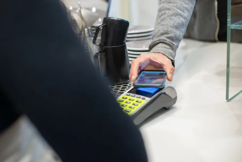 A customer makes a contactless payment using a smartphone at a café, showcasing modern digital transactions. (stock photo via Pexels)